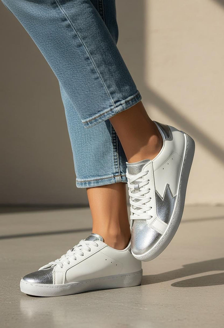 White sneakers with silver accents worn with blue jeans on a neutral background