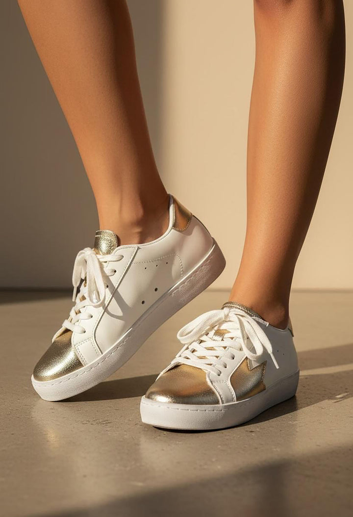 White sneakers with gold soles worn by a person on a neutral background