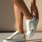 White sneakers with gold lace details worn by a person on a neutral background
