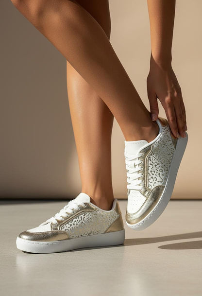 White sneakers with gold lace details worn by a person on a neutral background