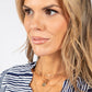 Woman wearing a striped shirt with layered necklaces against a plain background