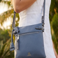 Person holding a blue crossbody bag with a blurred green background