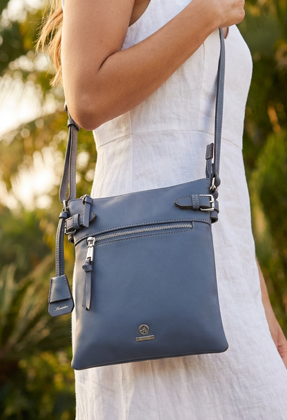 Person holding a blue crossbody bag with a blurred green background