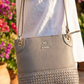 Gray handbag with woven texture held by a person against a blurred floral background