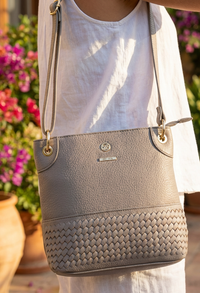 Gray handbag with woven texture held by a person against a blurred floral background