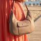 Woman holding a beige handbag on a wooden boardwalk with a blurred beach background