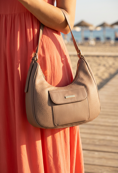 Woman holding a beige handbag on a wooden boardwalk with a blurred beach background
