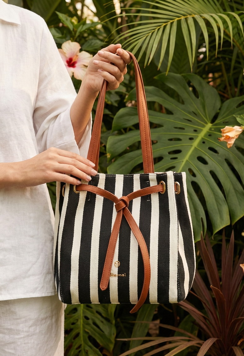 Person holding a black and white striped bag with brown leather straps against a green leafy background