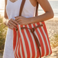 Woman holding a red and white striped bag on a beach