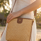 Person holding a woven handbag with a blurred natural background