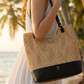 Person holding a woven handbag with a blurred beach background