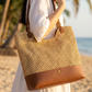 Person holding a woven handbag on a beach with palm trees in the background