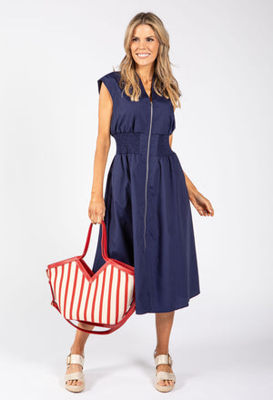 Woman in a navy dress holding a red and white striped bag on a white background