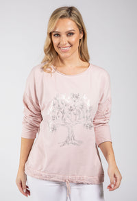 Woman wearing a pink long-sleeve top with a tree design on a plain background