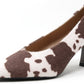 High-heeled shoe with brown and white cow print pattern on a white background