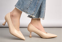 Beige high-heeled shoes worn with denim jeans on a neutral background