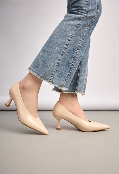 Beige high-heeled shoes worn with a denim skirt on a neutral background