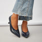 Black high-heeled shoes worn with blue jeans on a light gray background