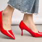 Red high-heeled shoes worn with a denim skirt on a neutral background