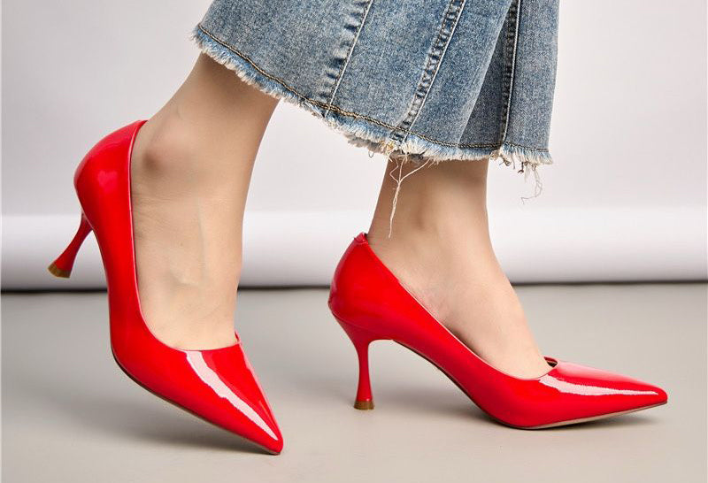 Red high-heeled shoes worn with a denim skirt on a neutral background