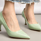 Light green high-heeled shoes worn by a person on a neutral background