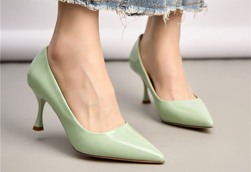 Light green high-heeled shoes worn by a person on a neutral background