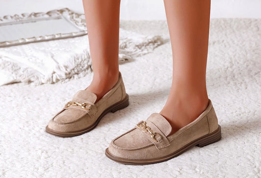 Beige loafers with gold chain details worn by a person on a light background