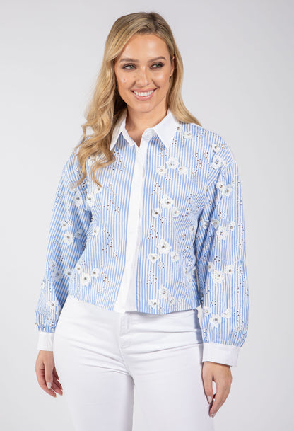 Woman wearing a blue and white floral embroidered shirt on a white background