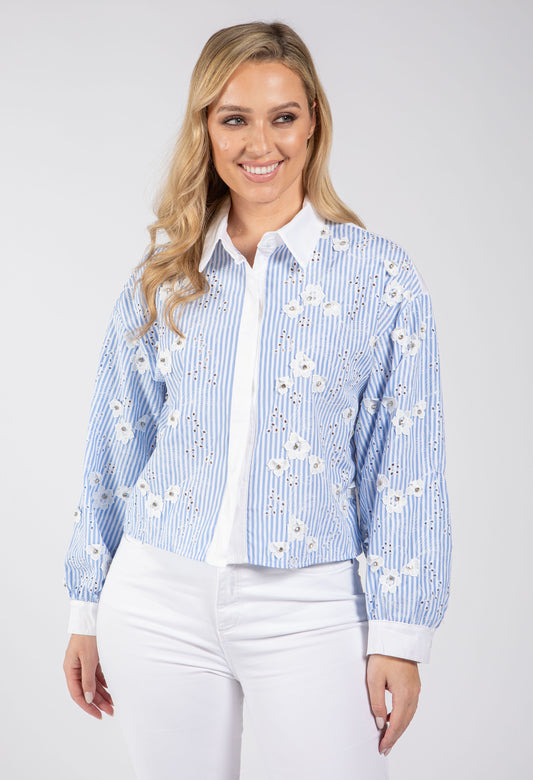 Woman wearing a blue and white floral embroidered shirt on a white background