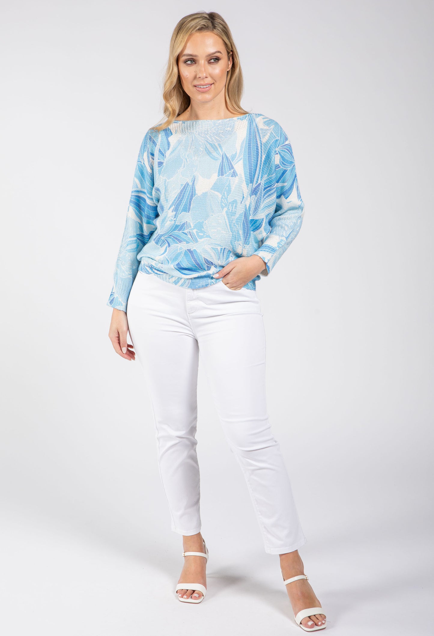 Woman wearing a blue tie-dye sweater and white pants on a white background
