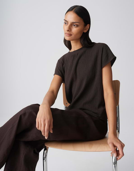 Woman sitting on a chair wearing a brown outfit against a plain background