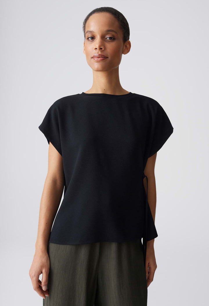 Woman wearing a black top and green pants against a plain background