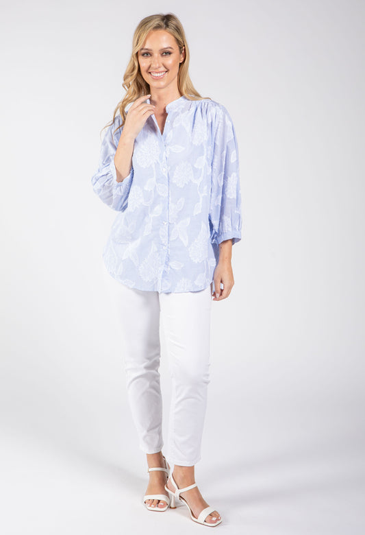 Woman wearing a light blue patterned blouse and white pants on a white background