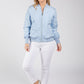 Woman wearing a light blue bomber jacket and white pants on a gray background