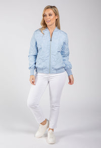 Woman wearing a light blue bomber jacket and white pants on a gray background