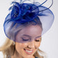 Woman wearing a blue decorative hat with feathers against a white background