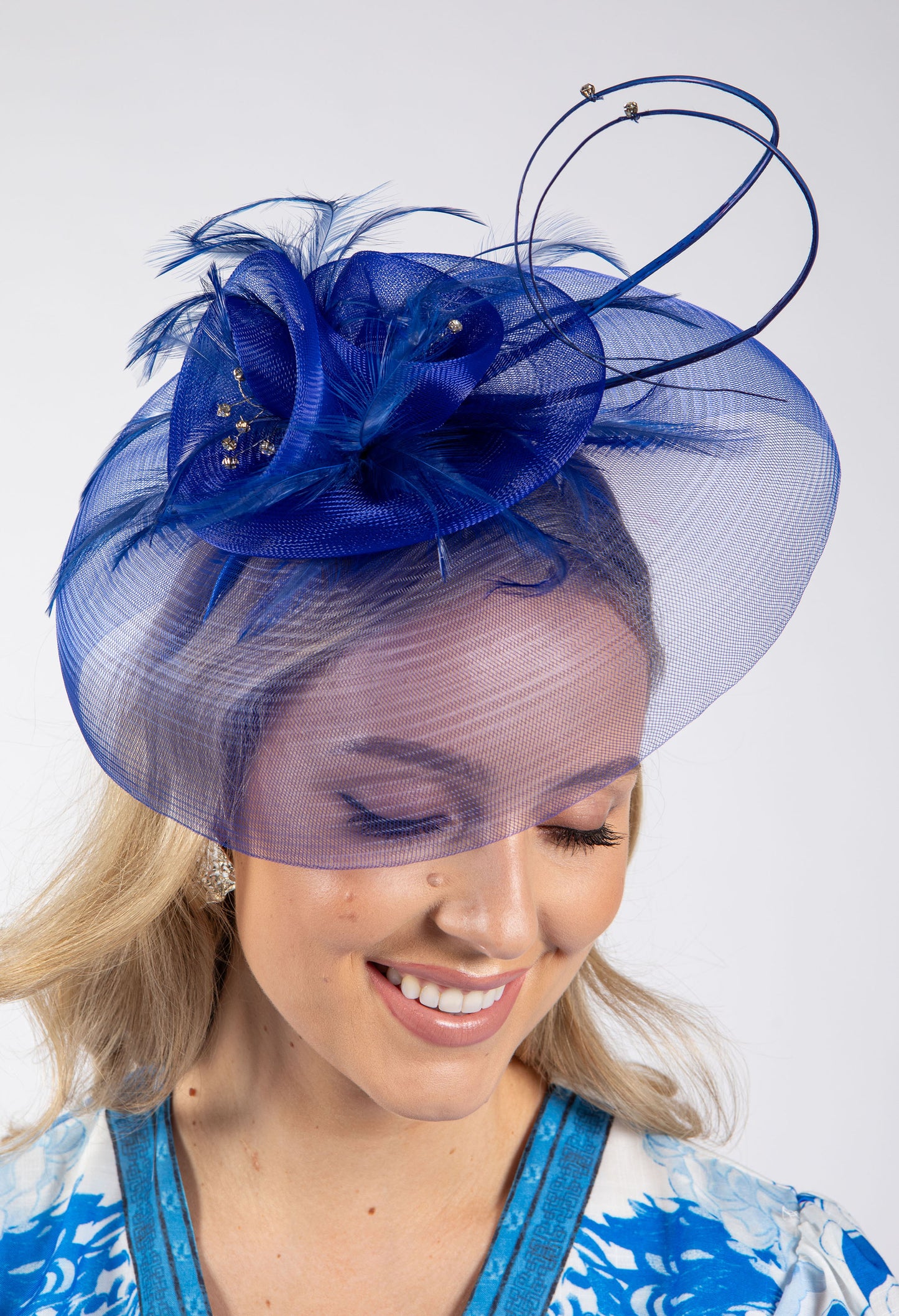 Woman wearing a blue decorative hat with feathers against a white background