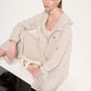 Woman wearing a beige outfit sitting on a white surface with a plain background