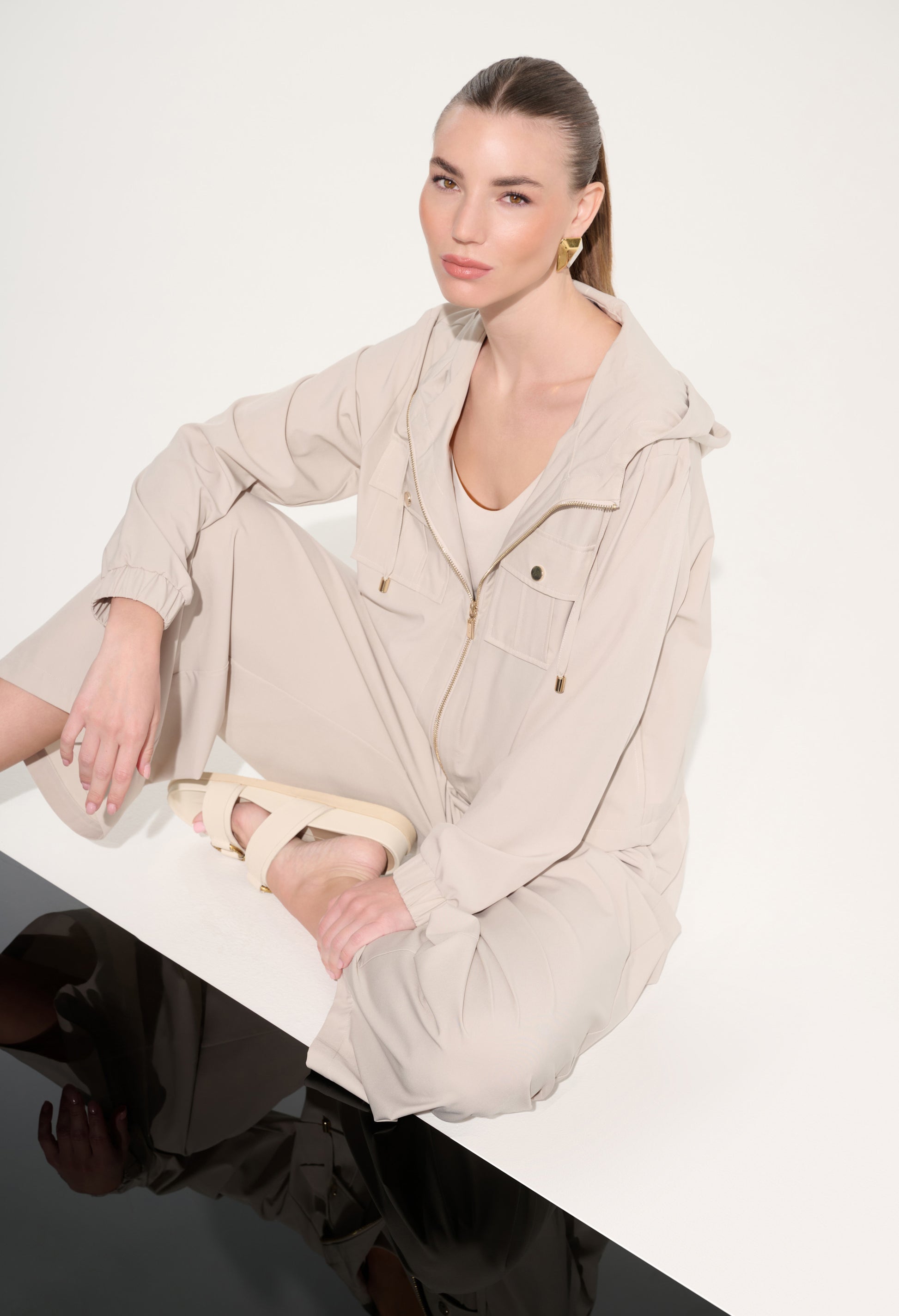 Woman wearing a beige outfit sitting on a white surface with a plain background