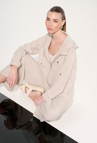 Woman wearing a beige outfit sitting on a white surface with a plain background