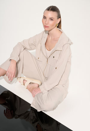 Woman wearing a beige outfit sitting on a white surface with a plain background