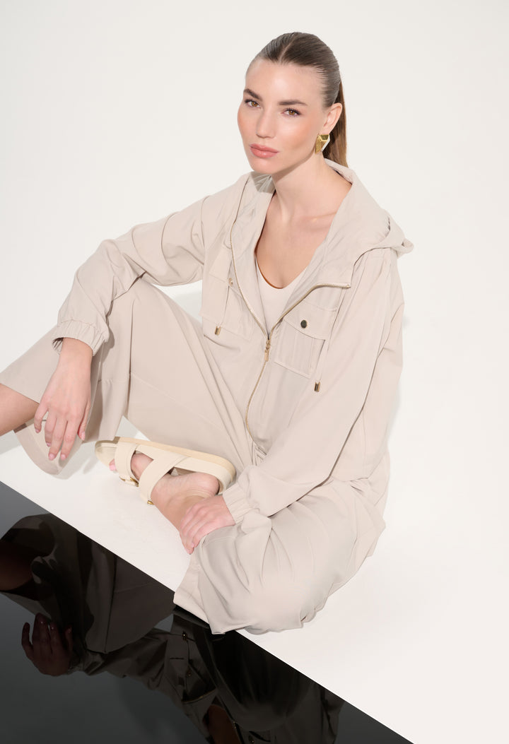 Woman wearing a beige outfit sitting on a white surface with a plain background
