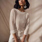 Woman wearing a beige knitted sweater and pants sitting on a chair against a plain background