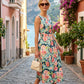 Woman in a floral dress walking down a picturesque street with mountains and water in the background.