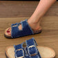 Denim sandals with buckles worn by a person on a wooden floor.