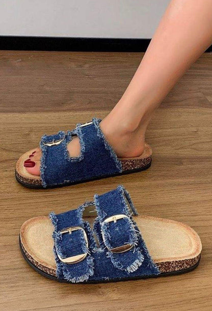 Denim sandals with buckles worn by a person on a wooden floor.
