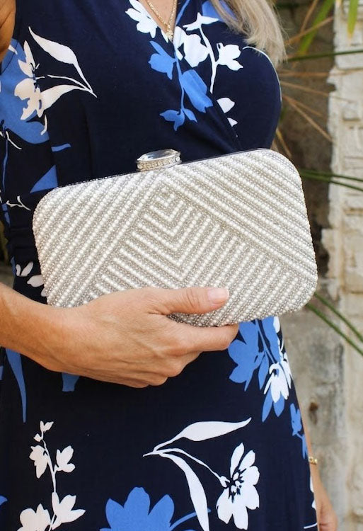 Person holding a silver beaded clutch with a floral dress in the background