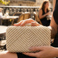 Person holding a gold clutch bag outdoors with blurred background