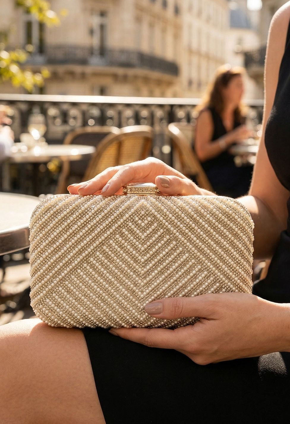 Person holding a gold clutch bag outdoors with blurred background