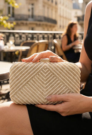Person holding a gold clutch bag outdoors with blurred background